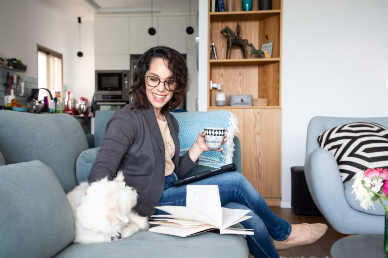 אלה שלוי אנטליס על ספה עם קפה, ספר וכלבה